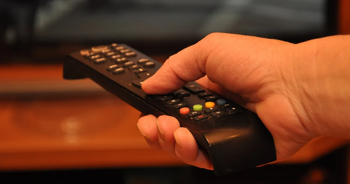 Mão segurando o controle remoto da TV durante o teste IPTV grátis da Barato IPTV